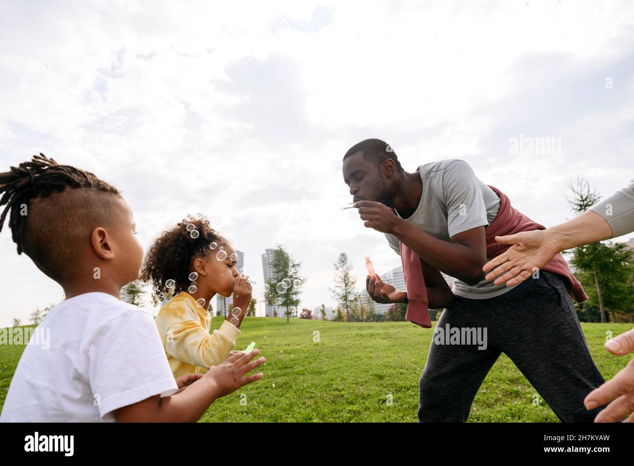 Le père soufflait de bulles tout en jouant avec les enfants dans le parc Banque D'Images