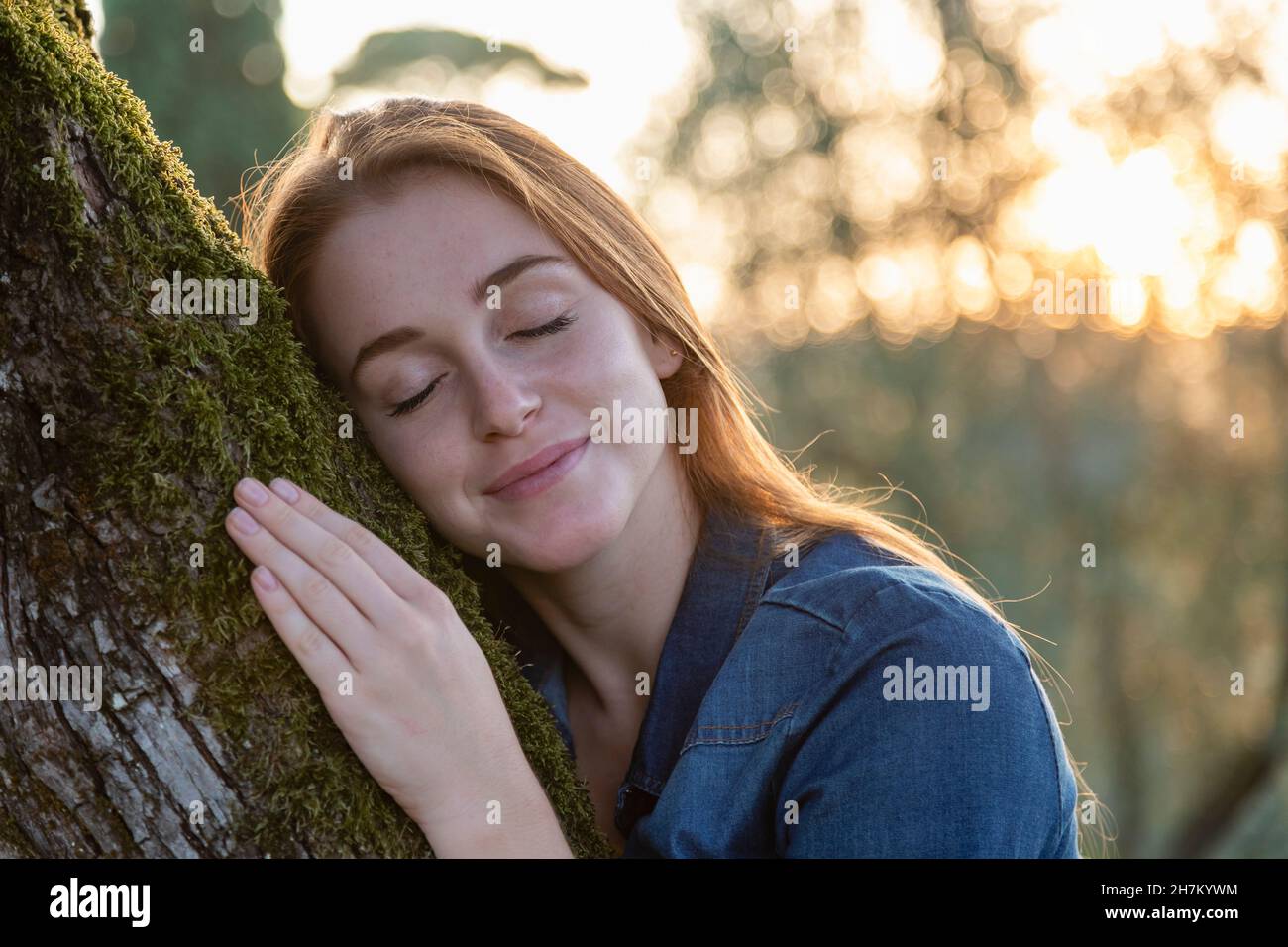 Femme avec les yeux fermés embrassant l'arbre au coucher du soleil Banque D'Images