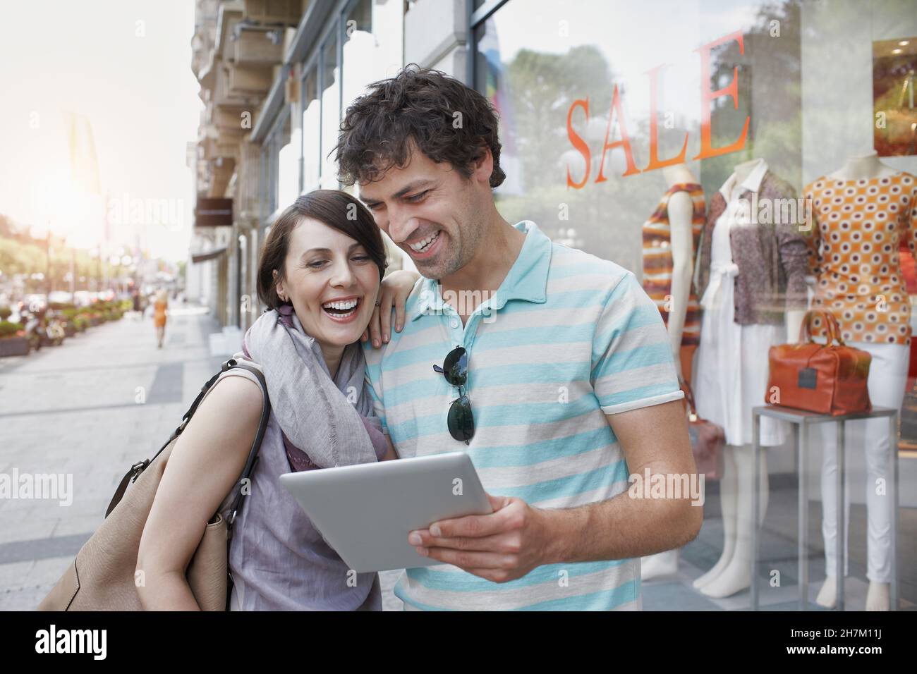 Couple joyeux utilisant une tablette numérique en se tenant près d'un magasin de vêtements Banque D'Images