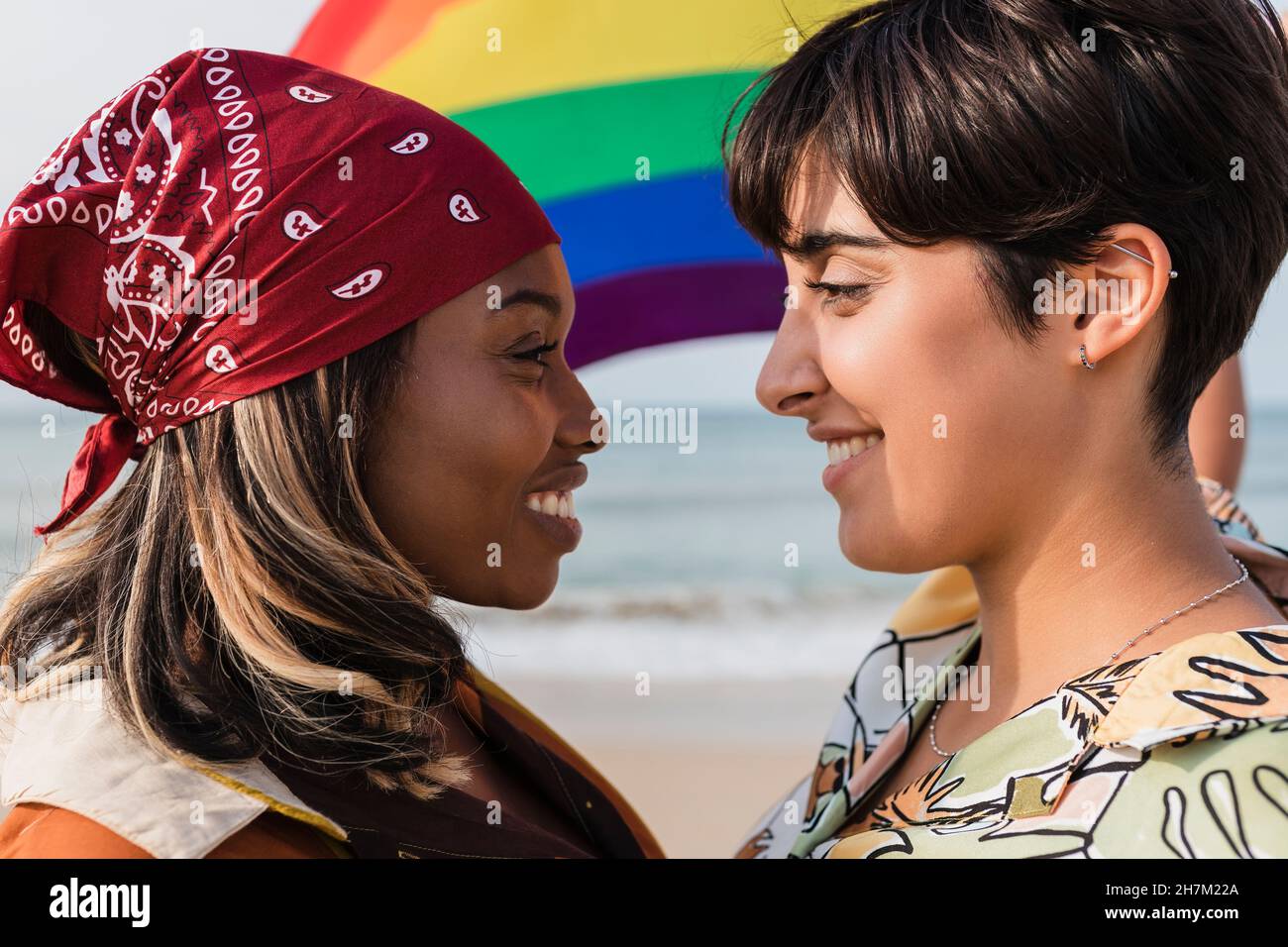 Couple lesbien romantique avec drapeau arc-en-ciel se regardant les uns les autres à la plage Banque D'Images