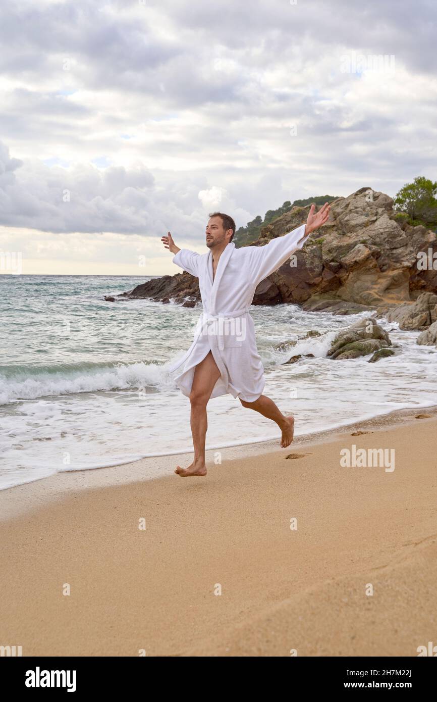 Homme insouciant dans le peignoir de course avec les bras étendus à la plage Banque D'Images