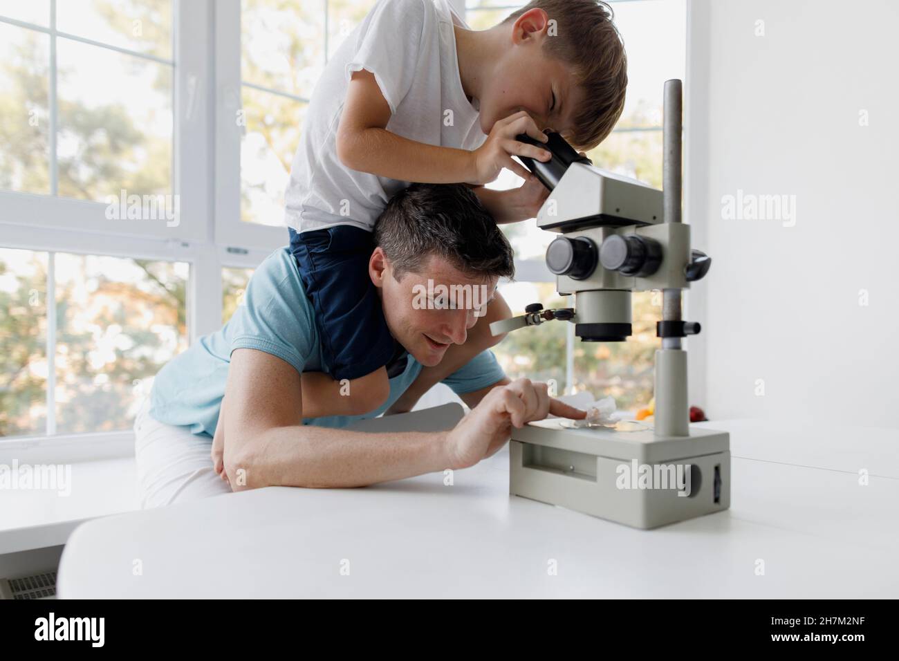 Curieux garçon utilisant un microscope tout en étant assis sur les épaules du père à la maison Banque D'Images