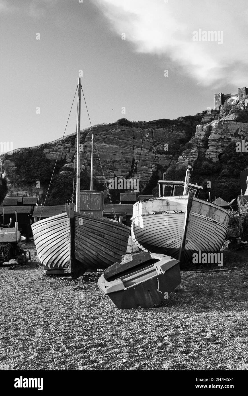 Un bateau de pêche traditionnel en bois s'assoit sur la rive de la mer en galets de la plage de Rock A Nore, avec des falaises de grès et un funiculaire en arrière-plan, Banque D'Images
