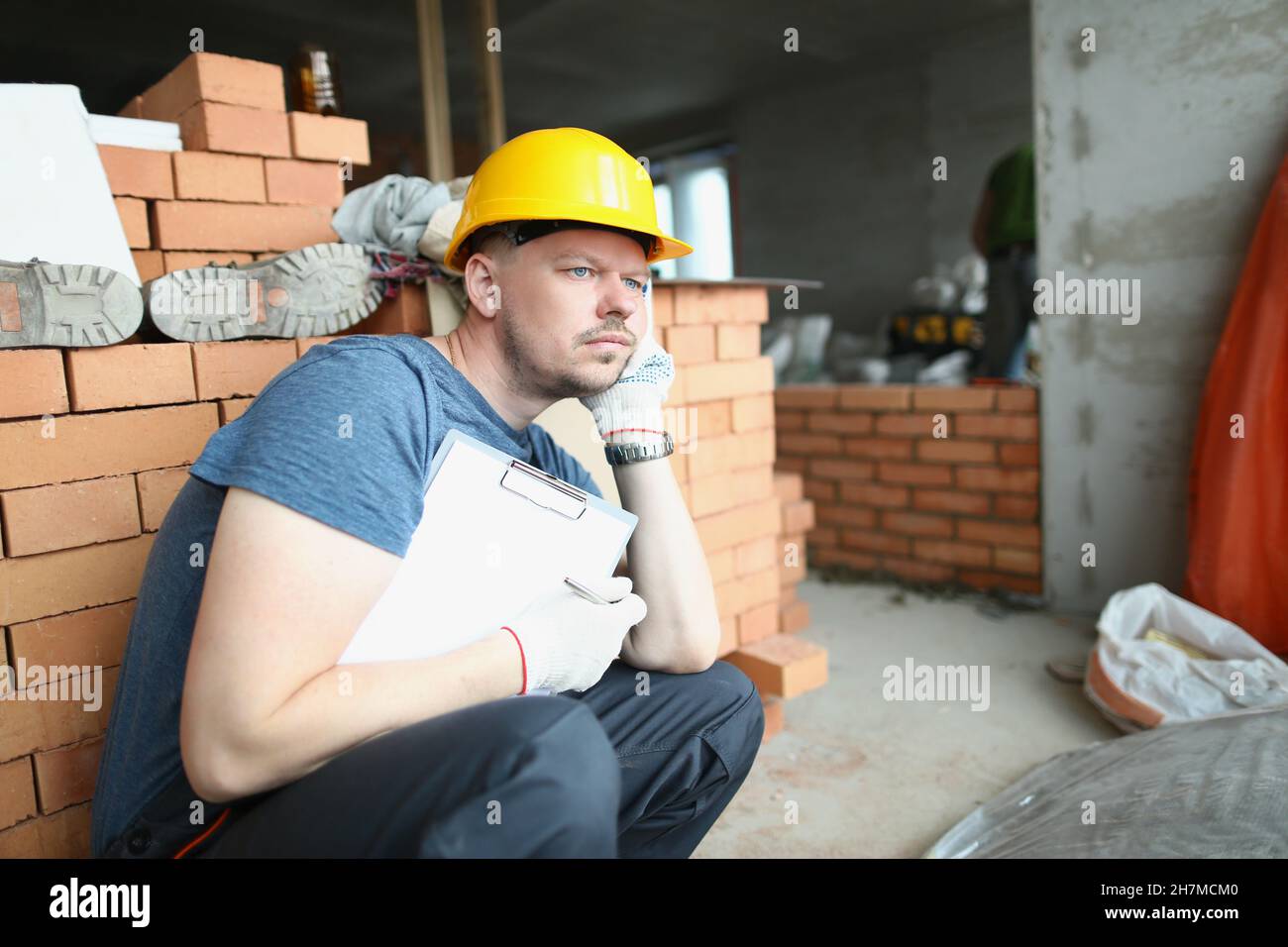 Le travailleur contrarié s'assoit entouré d'un site de construction en désordre avec du papier Banque D'Images