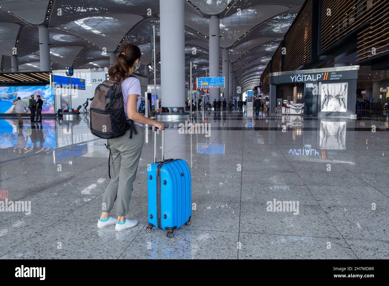 ISTANBUL, TURQUIE - 7 septembre 2021 : une femme tire une valise bleue dans le terminal de l'aéroport d'Istanbul.Fille itinérante portant des vêtements décontractés et un masque avec Banque D'Images