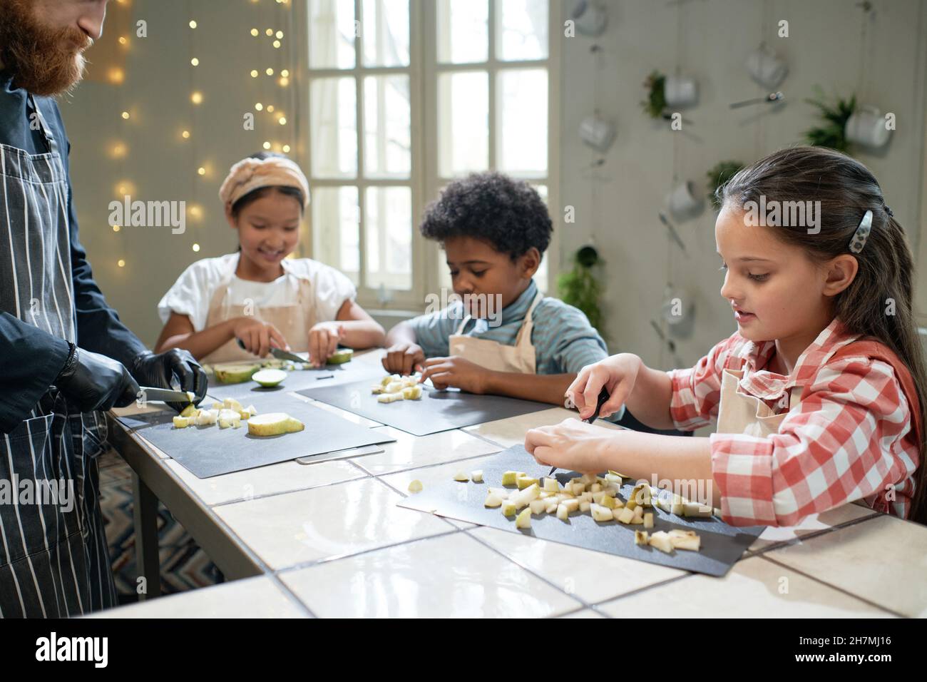 Groupe d'enfants apprenant à couper des fruits à la table avec le chef pendant une leçon Banque D'Images