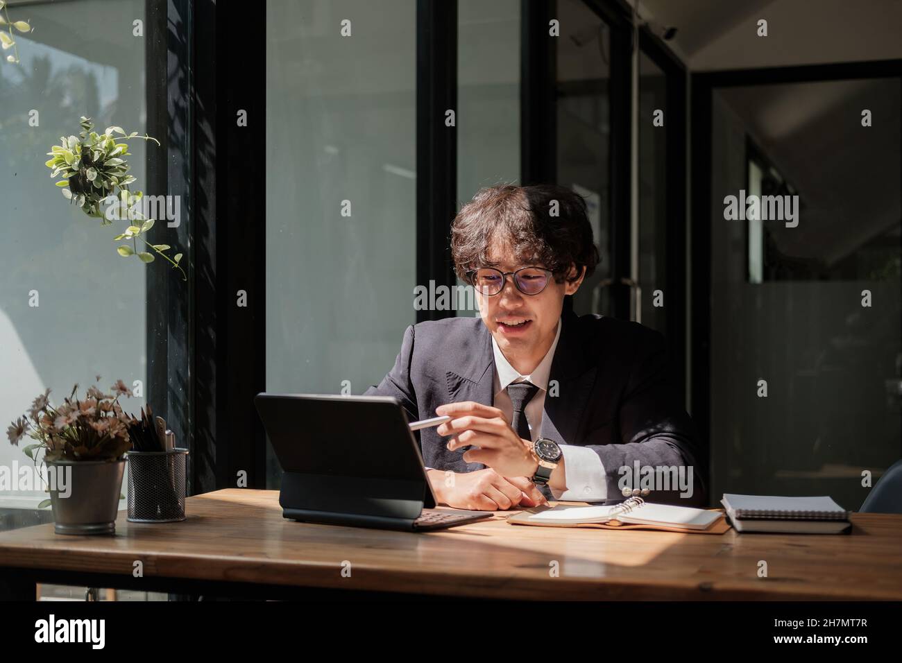 Jeune homme d'affaires asiatique en lunettes travaillant à distance avec une tablette numérique, assis à une table en bois dans un café.Agréable homme heureux communiquant dans le social Banque D'Images
