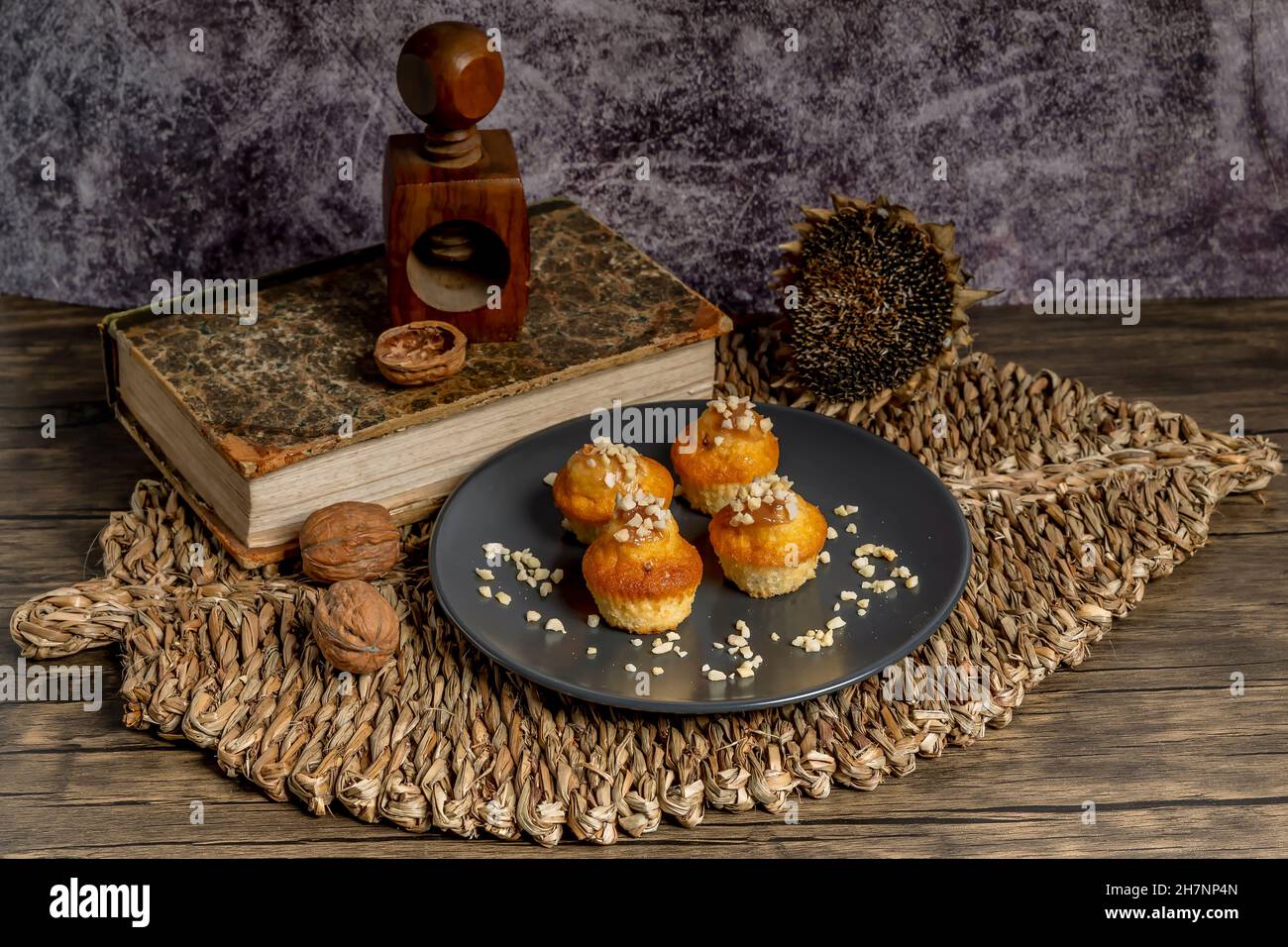Petits muffins recouverts d'amandes hachées sur une assiette grise, avec un napperon en osier et un casse-noisette en bois Banque D'Images