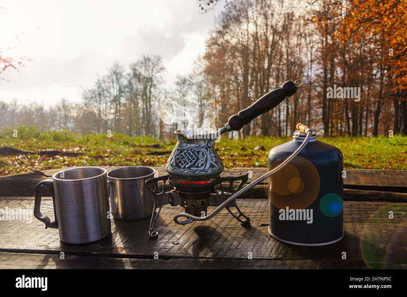 Faire bouillir la glace de café sur le brûleur portable et les tasses en métal sur la table en bois. Faire des boissons chaudes en plein air dans le parc. Banque D'Images