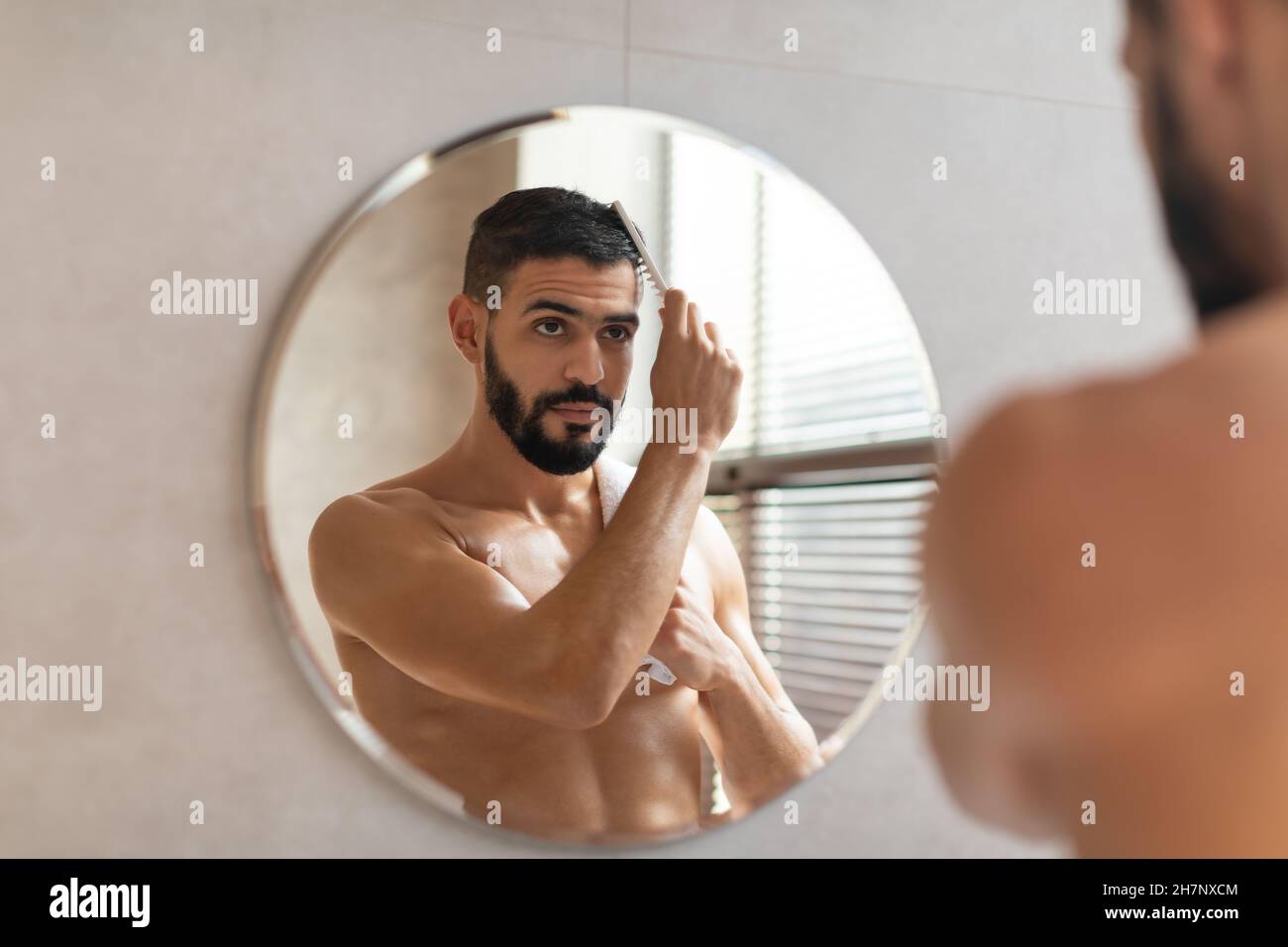 Vue arrière de l'homme regardant dans le miroir se brossant les cheveux Banque D'Images