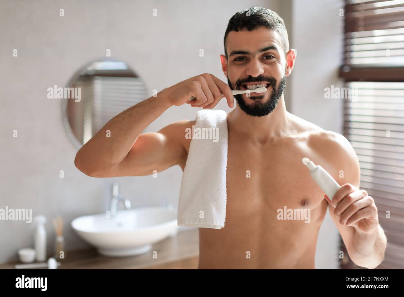 Joyeux jeune homme arabe utilisant la brosse à dents dans la salle de bains Banque D'Images
