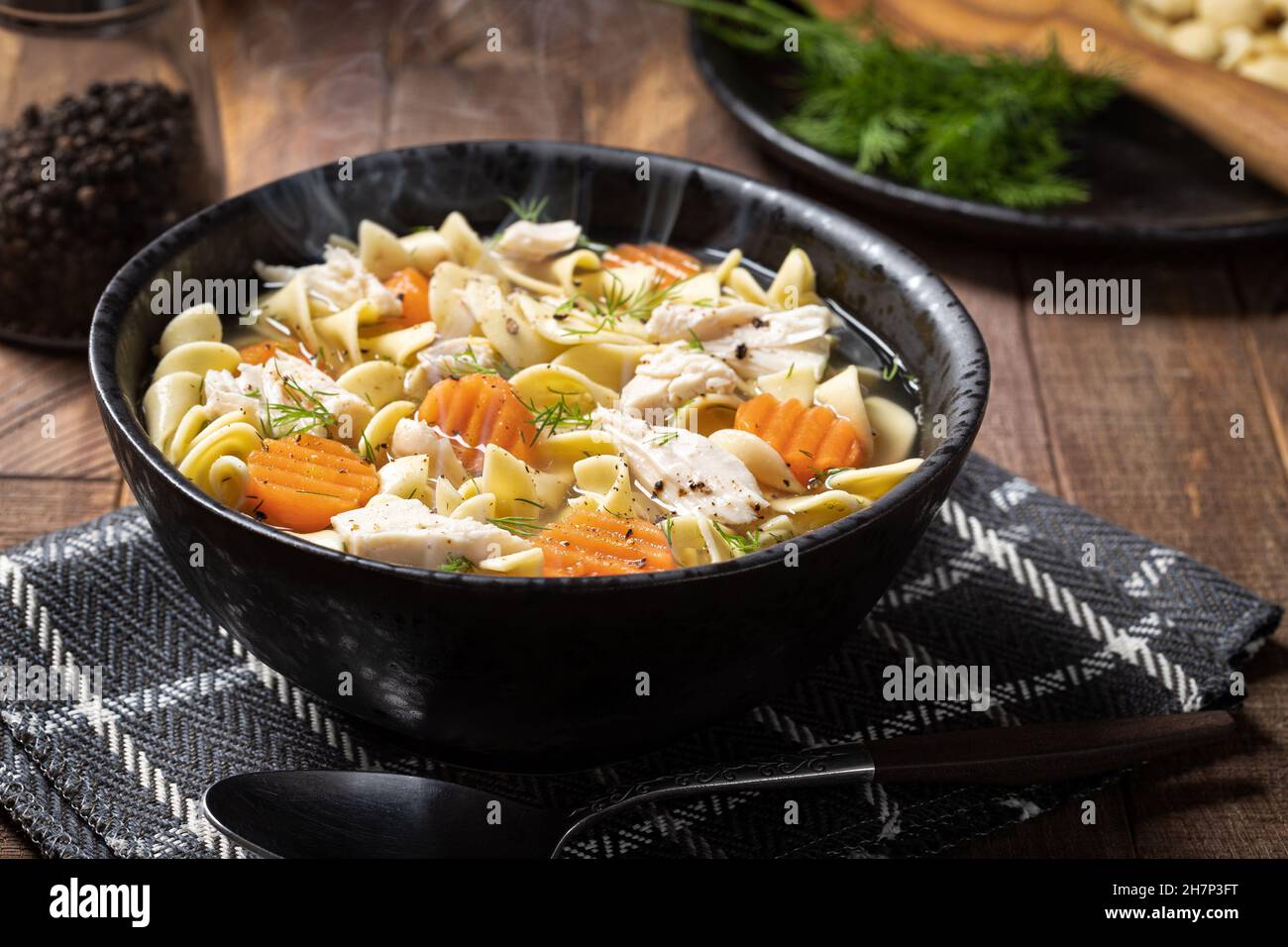 Bol vapeur de soupe de nouilles de poulet avec carottes et aneth sur une table rustique en bois Banque D'Images