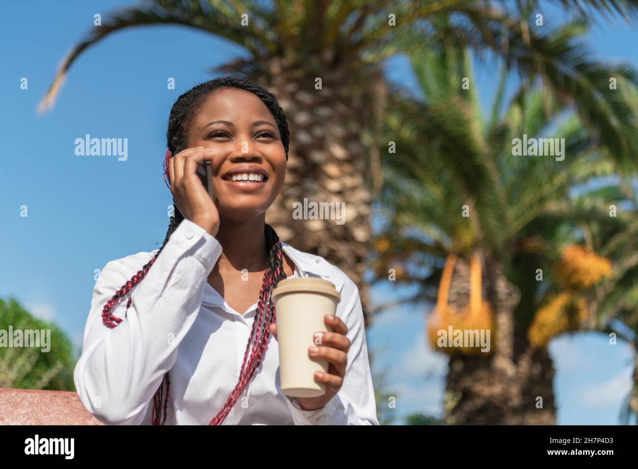 Femme afro-américaine souriante parlant avec mobile avec un café à emporter à la main Banque D'Images