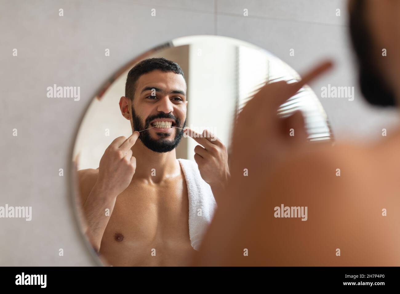 Jeune homme arabe utilisant sa soie dentaire dans la salle de bains Banque D'Images