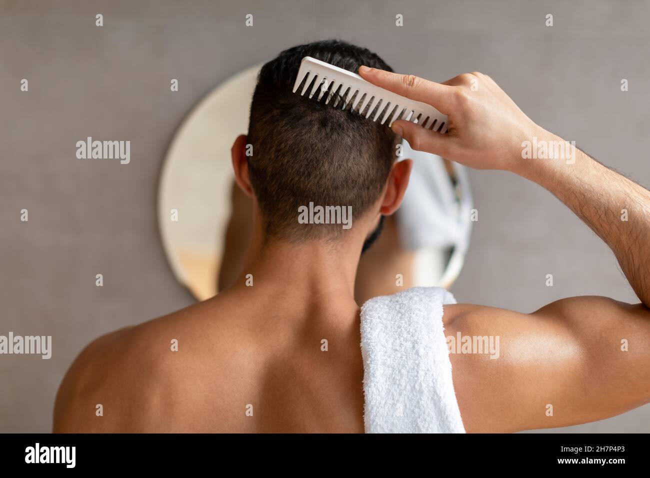 Vue arrière d'un jeune homme regardant dans le miroir se brossant les cheveux Banque D'Images