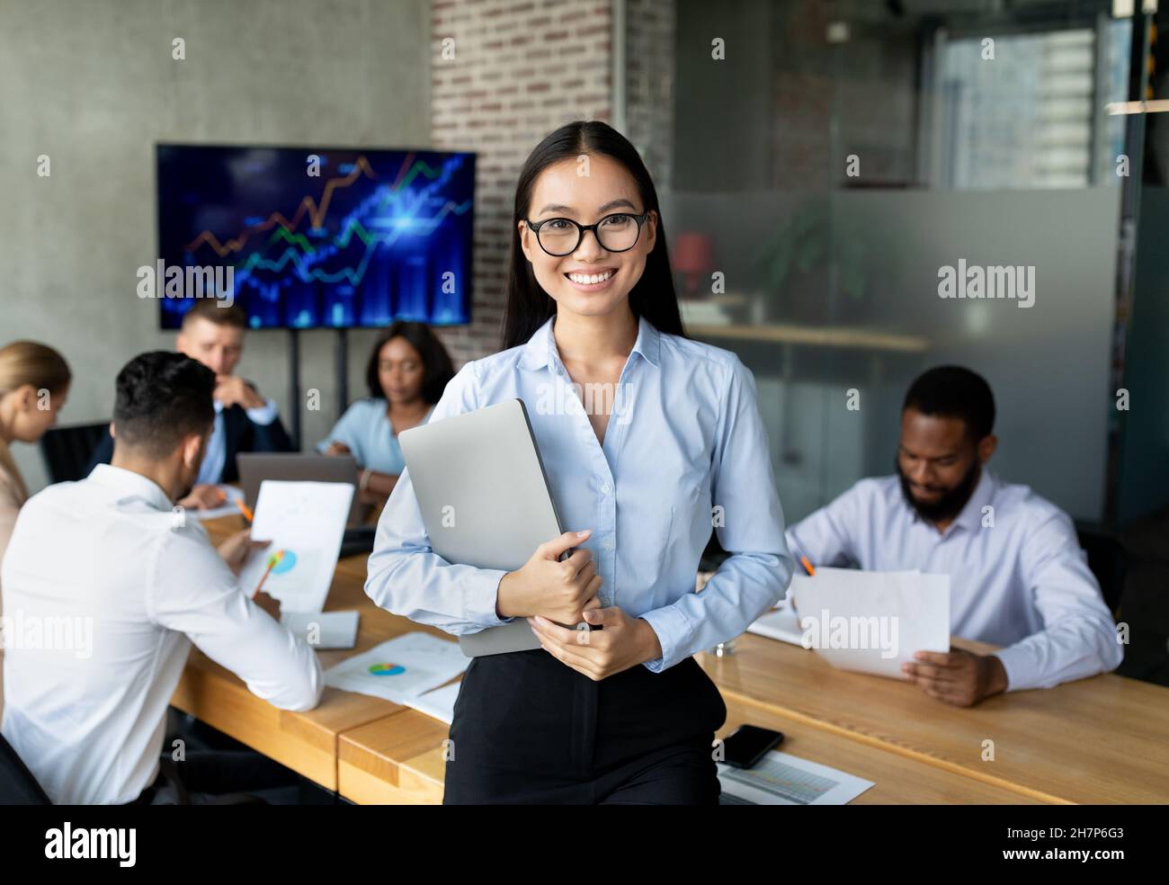 Une femme asiatique souriante pose à l'intérieur du bureau lors d'une réunion avec des collègues Banque D'Images