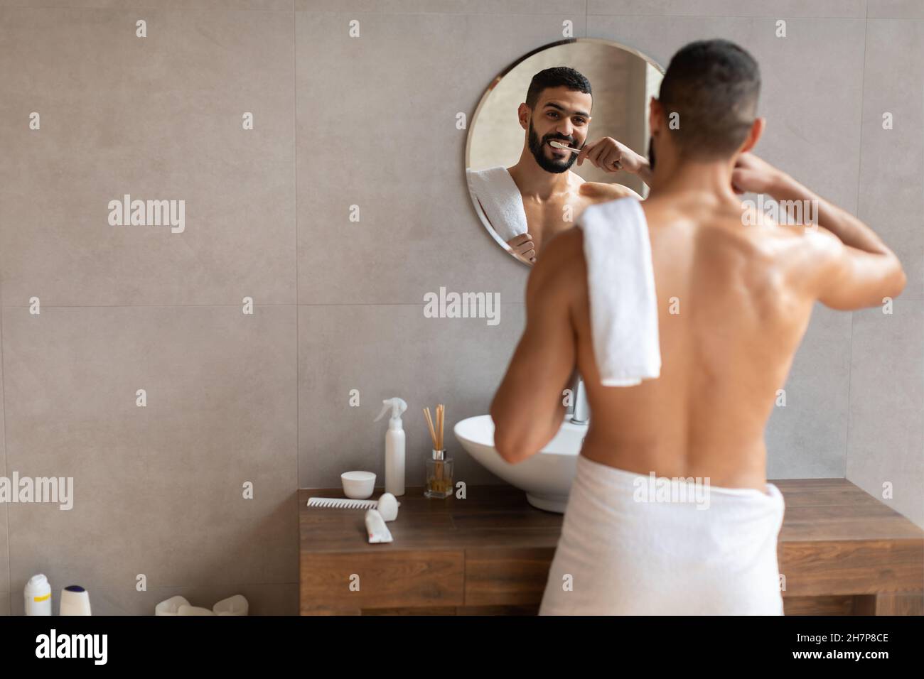 Joyeux jeune homme arabe utilisant la brosse à dents dans la salle de bains moderne Banque D'Images