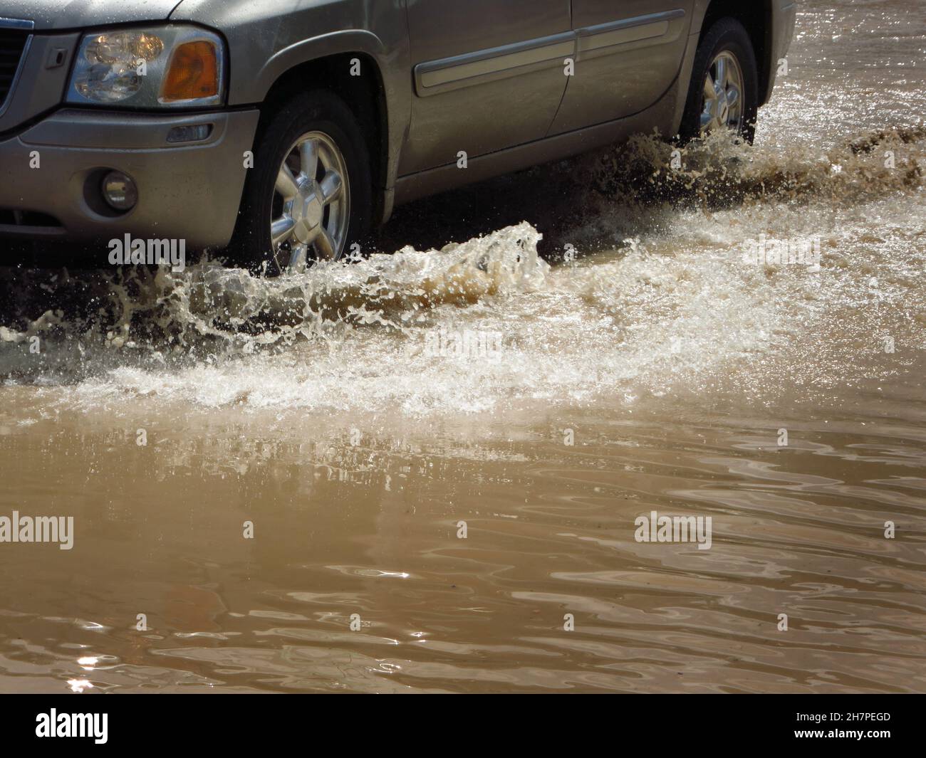 La voiture traverse une rue inondée avec des pneus éclaboussant de l'eau Banque D'Images
