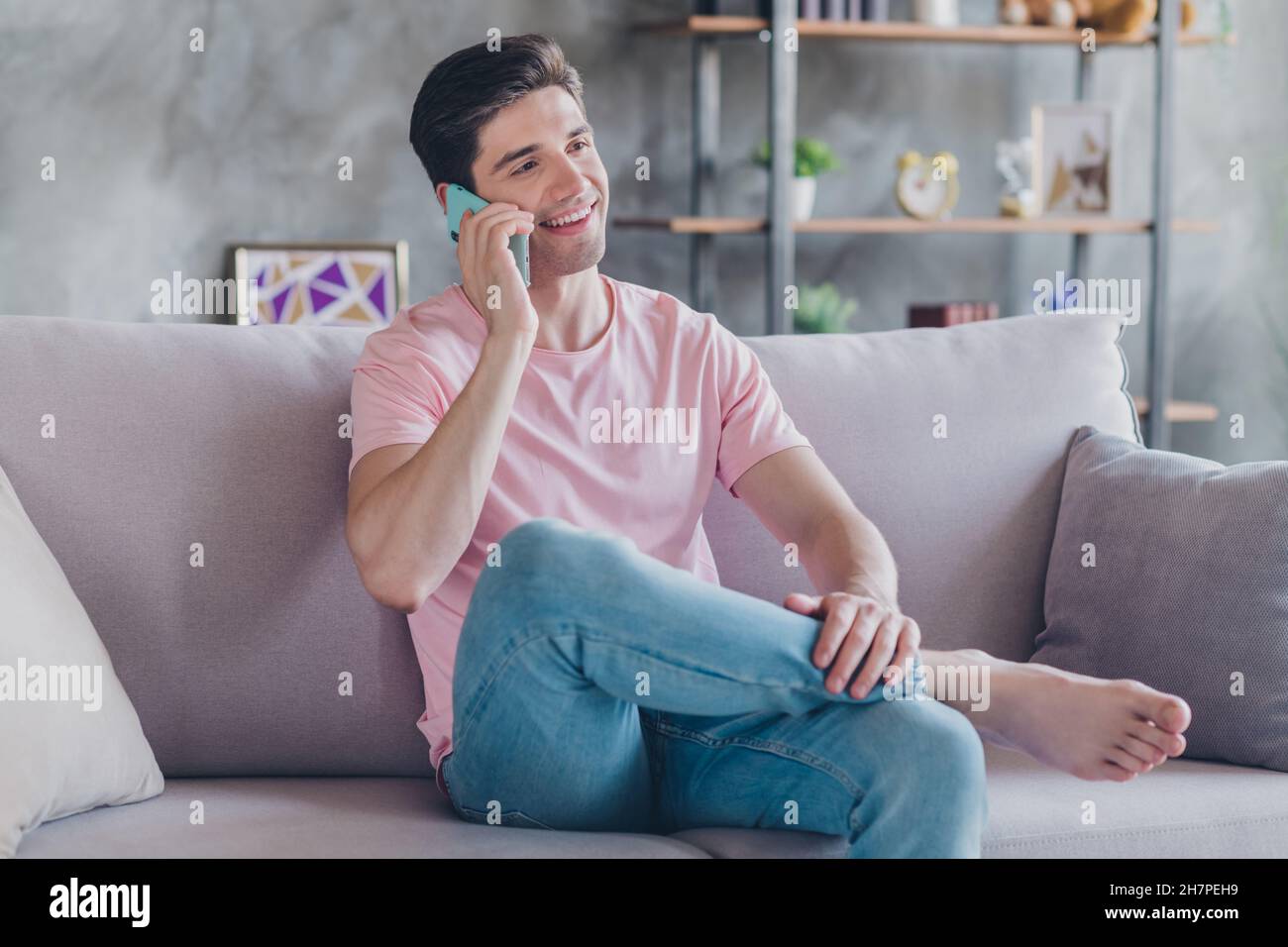 Portrait d'un sympathique gars gai assis sur un divan parlant au téléphone passer du temps libre vacances de discuter à l'intérieur Banque D'Images