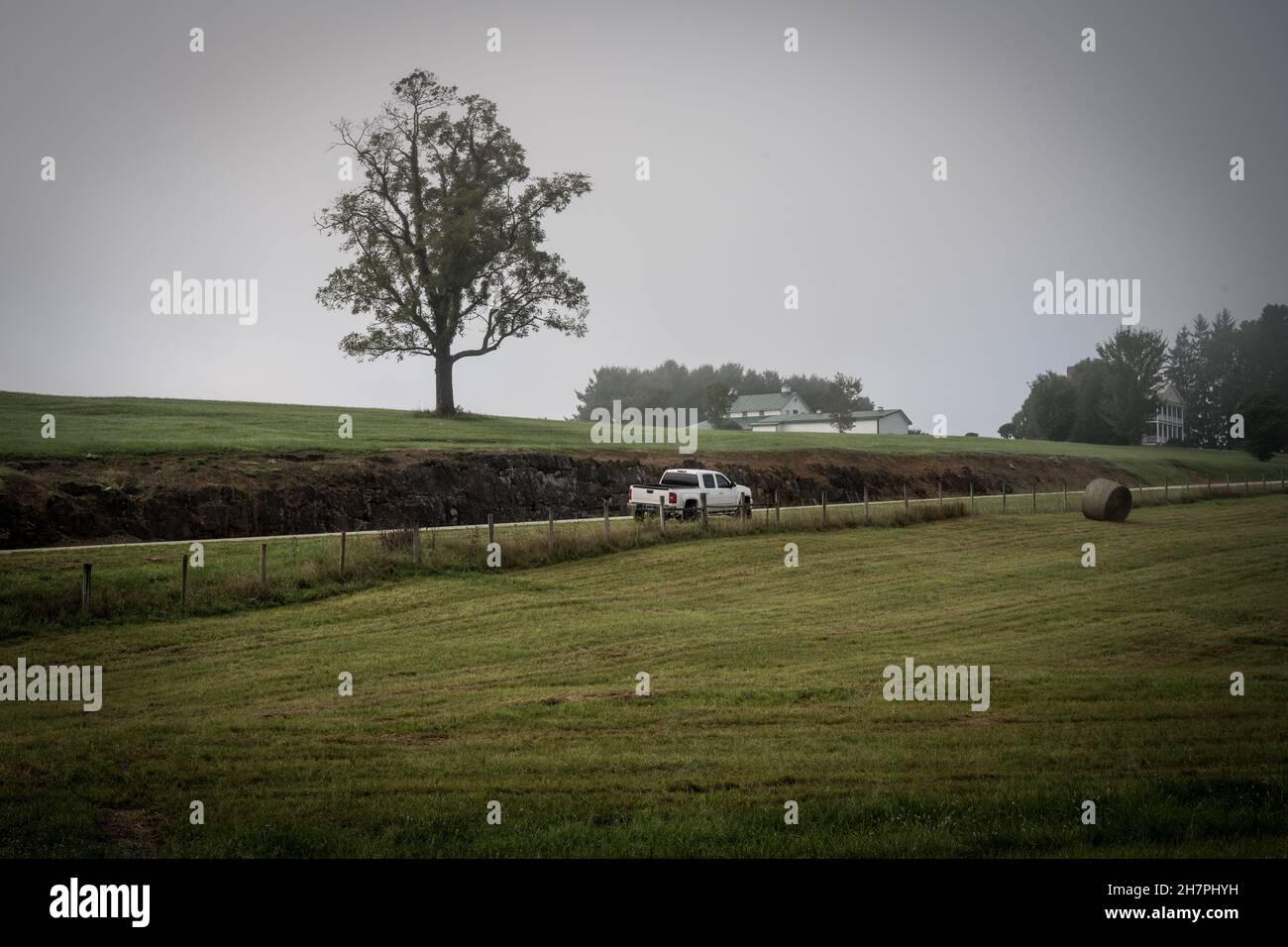 Photo d'un pick-up blanc à cheval sur une ferme enveloppée de brouillard. Banque D'Images