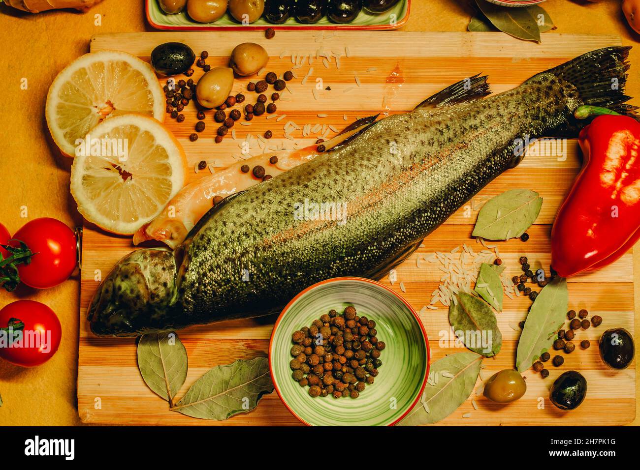 Vue de dessus du poisson frais sur une planche en bois avec beaucoup d'ingrédients citron, poivre, tomates et olives Banque D'Images