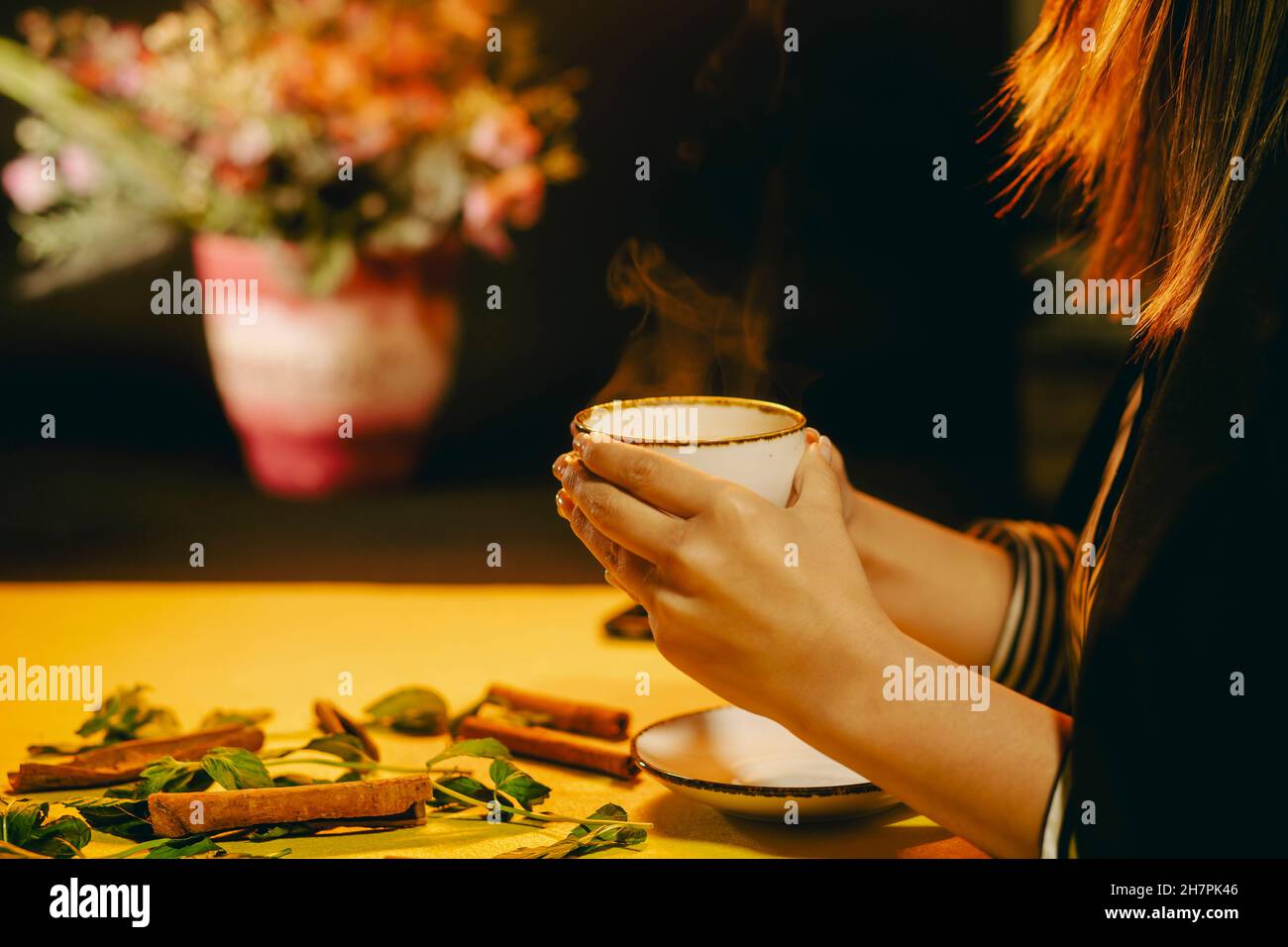 Ambiance thé chaud.Femme tenant une tasse de thé chaud fraîchement infusé et prête à boire.Encore la vie de thé avec des fleurs fraîches derrière Banque D'Images