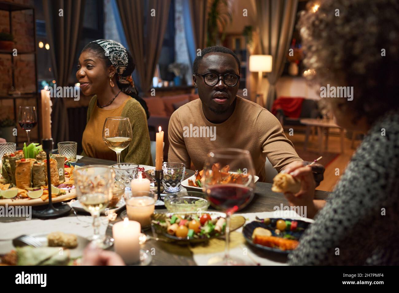 Un jeune homme africain en lunettes parlant à ses amis pendant le dîner à la table Banque D'Images