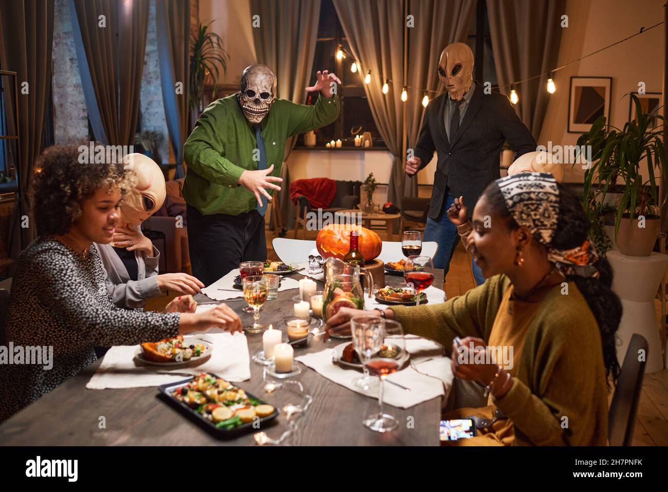 Groupe de personnes en costumes effrayants assis à table de salle à manger et célébrant les vacances d'Halloween à la maison Banque D'Images
