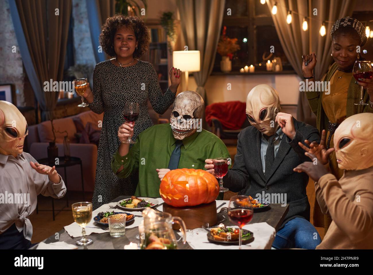 Groupe de gens heureux dans des masques effrayants boire du vin rouge pendant la fête d'Halloween à la maison Banque D'Images