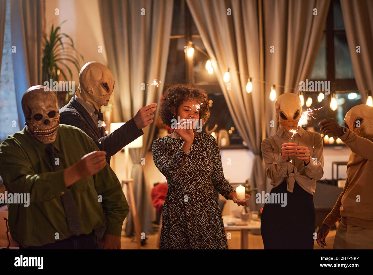 Groupe de personnes dans des masques effrayants tenant des spameurs et dansant pendant la fête d'Halloween Banque D'Images
