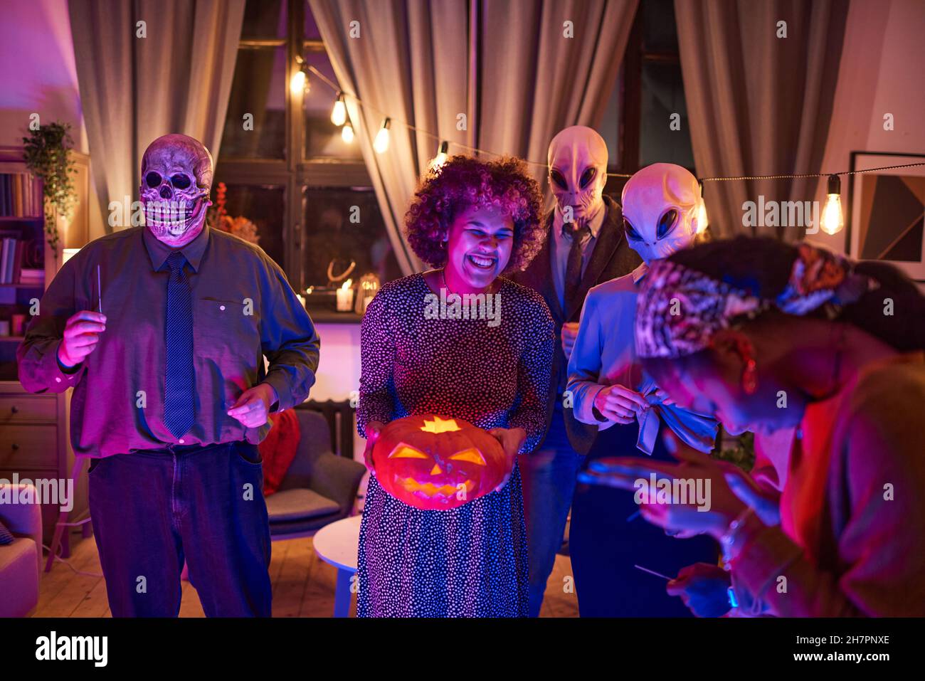 Femme africaine tenant la citrouille illuminée et s'amusant avec ses amis à la fête d'Halloween à la maison Banque D'Images