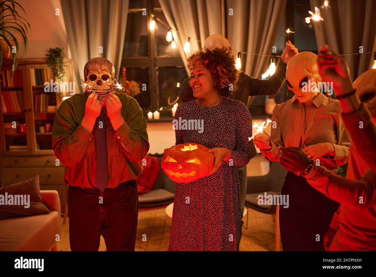 Groupe d'amis heureux célébrant la fête d'Halloween ensemble, ils portent des costumes et éclairent la citrouille à la maison Banque D'Images