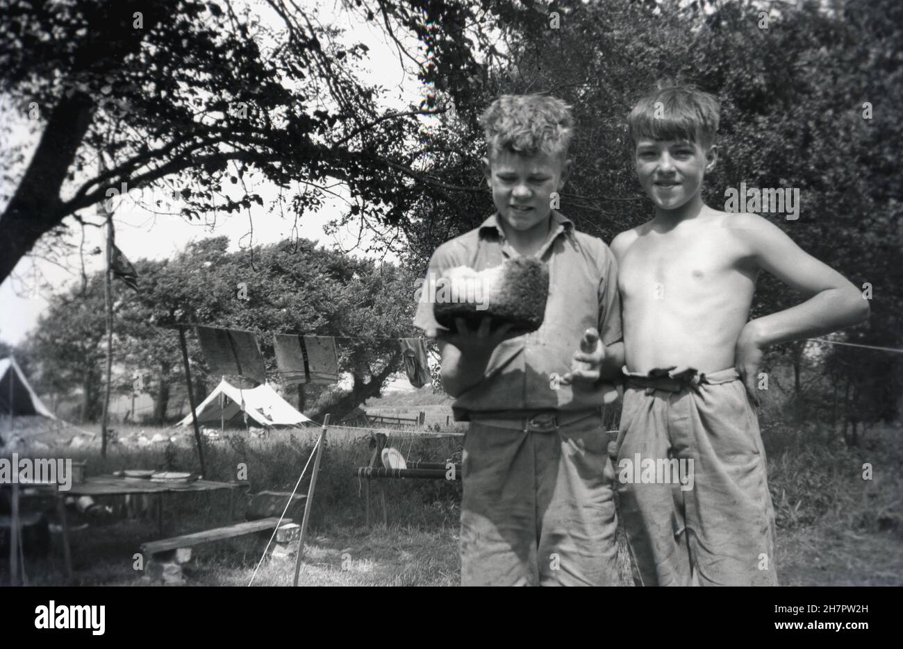 1938, historique, camp de scouts, debout ensemble à l'extérieur, deux jeunes cub souts ou hiboux, avec un pudding de riz - trop cuit!- fabriqué dans la cuisine du camp, Angleterre, Royaume-Uni. Banque D'Images