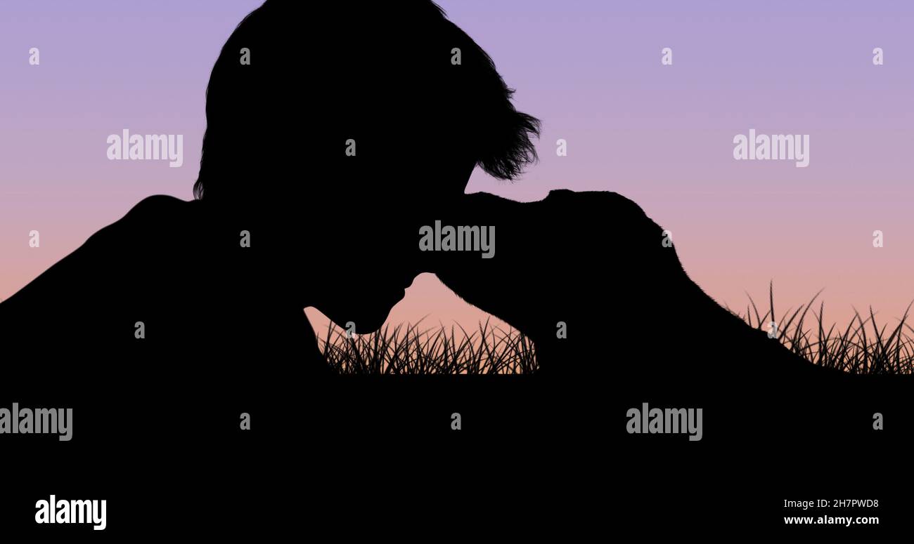 Silhouette de garçon allongé sur l'herbe tout en tenant le chiot au crépuscule contre le ciel clair avec l'espace de copie Banque D'Images