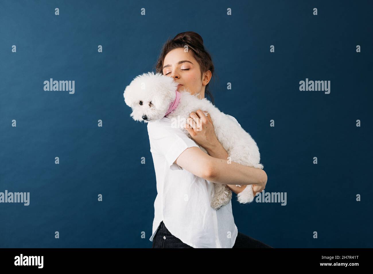 Jeune femme tenant son petit chien blanc en studio sur fond bleu Banque D'Images