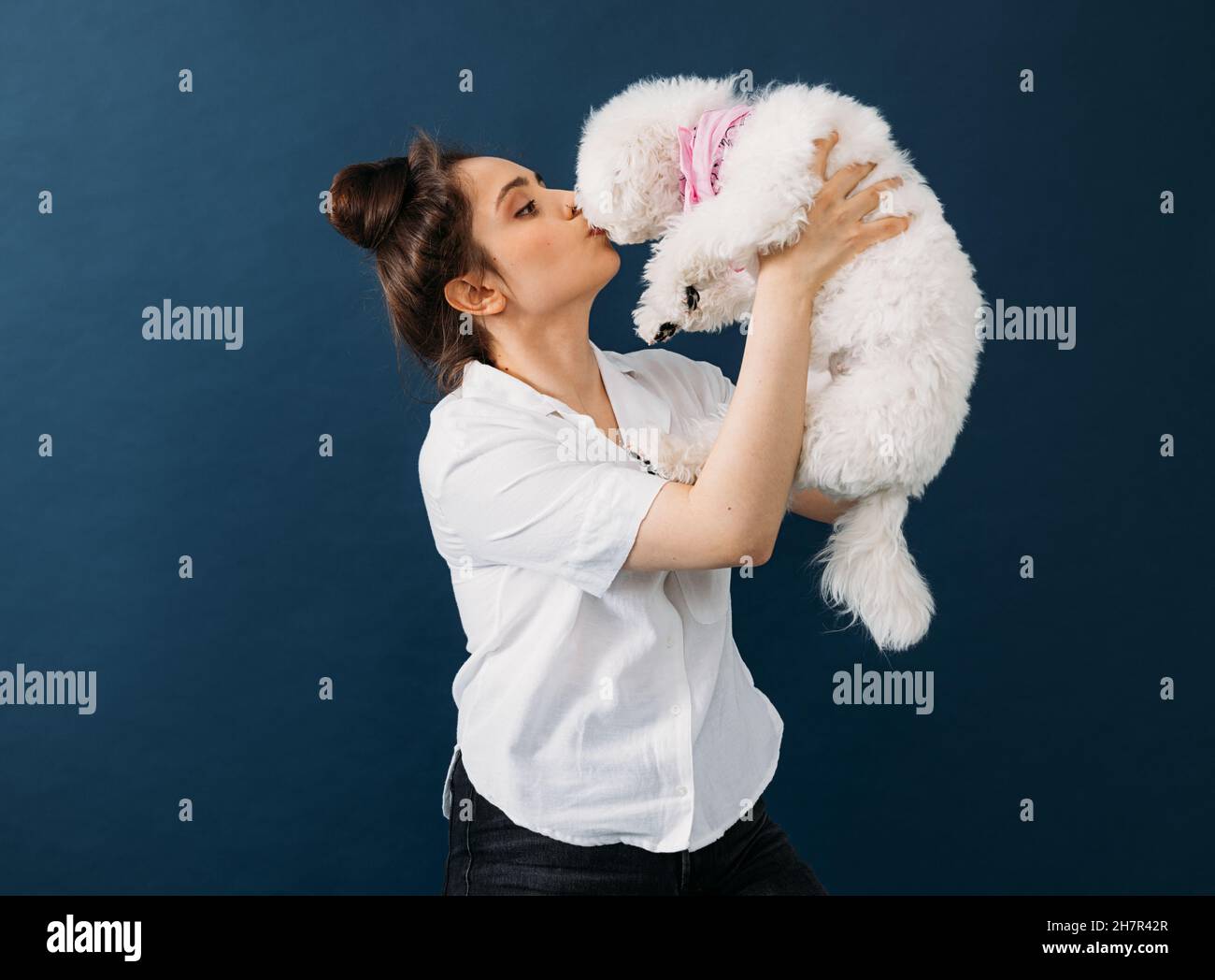 Vue latérale d'une femme tenant et embrassant son petit chien blanc en studio Banque D'Images