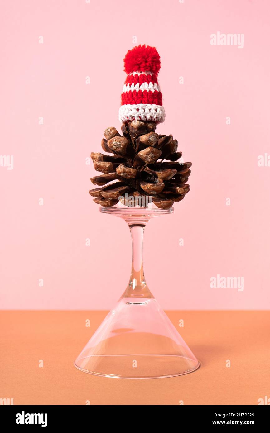 Verre martini inversé avec pinecone (Pinus Pinea) et chapeau de Santa sur fond rose.Photo verticale Banque D'Images