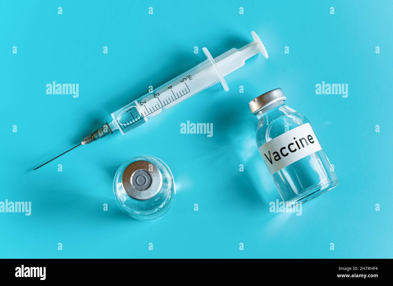 Flacons en verre avec étiquette de vaccin et aiguille de seringue hypodermique à proximité, vue du dessus sur fond cyan Banque D'Images