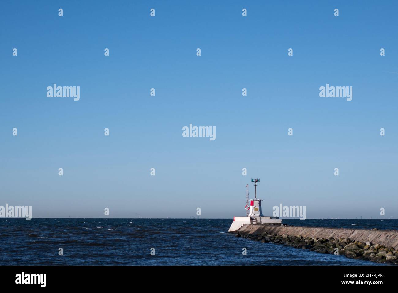 Un phare blanc et rouge situé sur un quai en pierre et une pause à vagues à l'entrée du port de Lomma Suède Banque D'Images