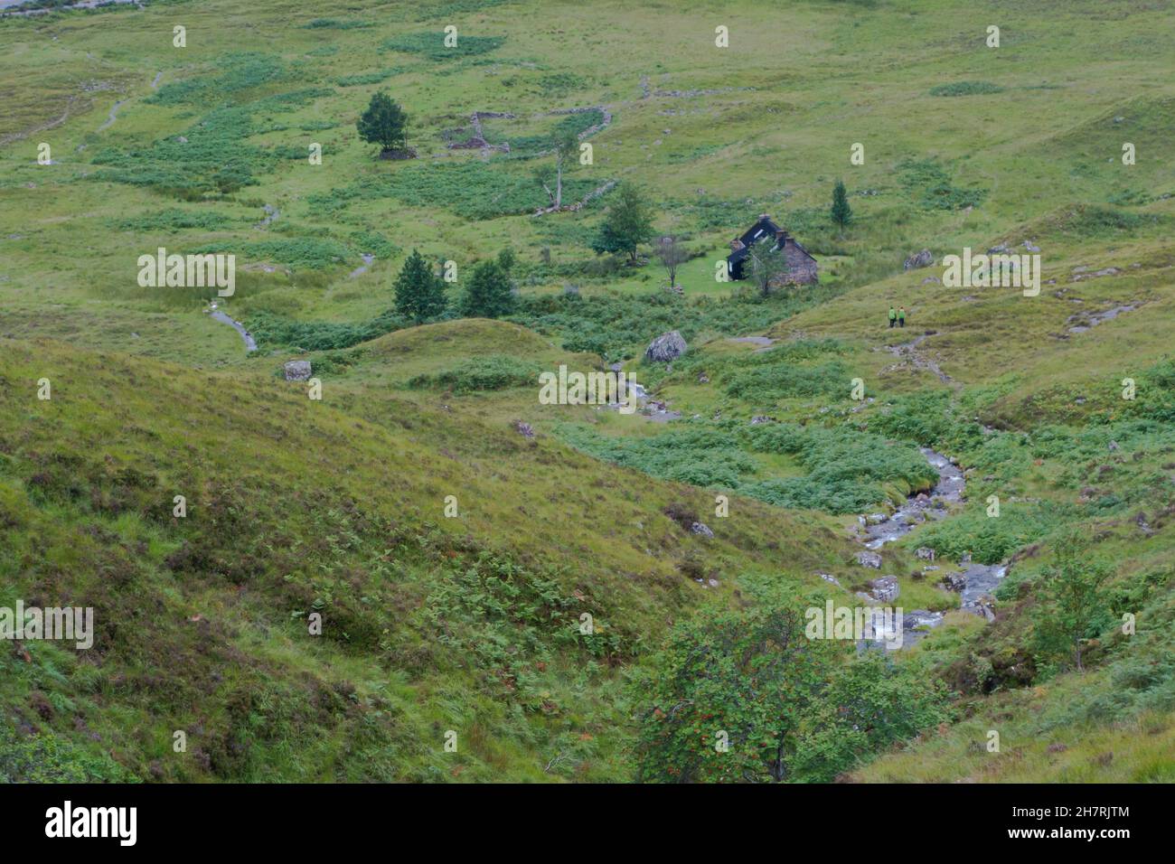 Deux randonneurs en équipement de pluie et sacs à dos marchant le long de la piste à travers la végétation verte chinée approchant le refuge en terre de Shenevall dans Fisherfield F Banque D'Images