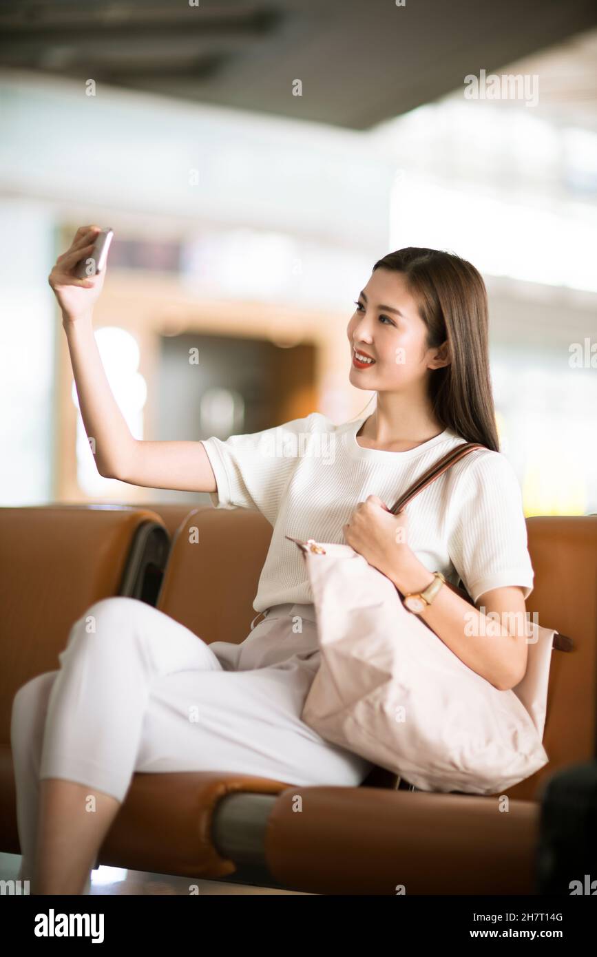 Un jeune couple prend des selfies sur son téléphone portable dans un salon d'aéroport Banque D'Images