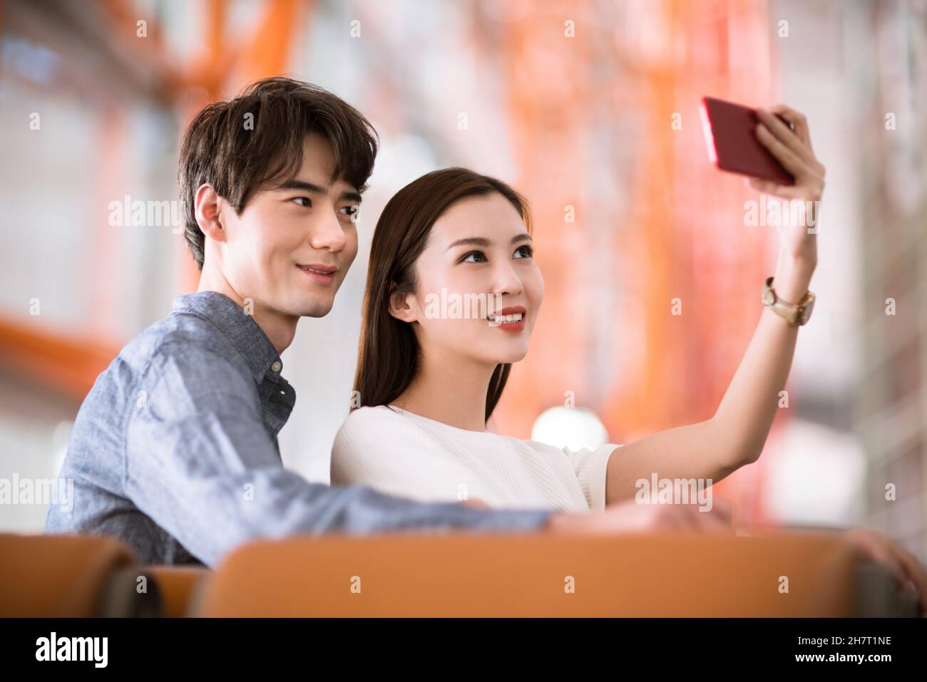 Un jeune couple prend des selfies sur son téléphone portable dans un salon d'aéroport Banque D'Images