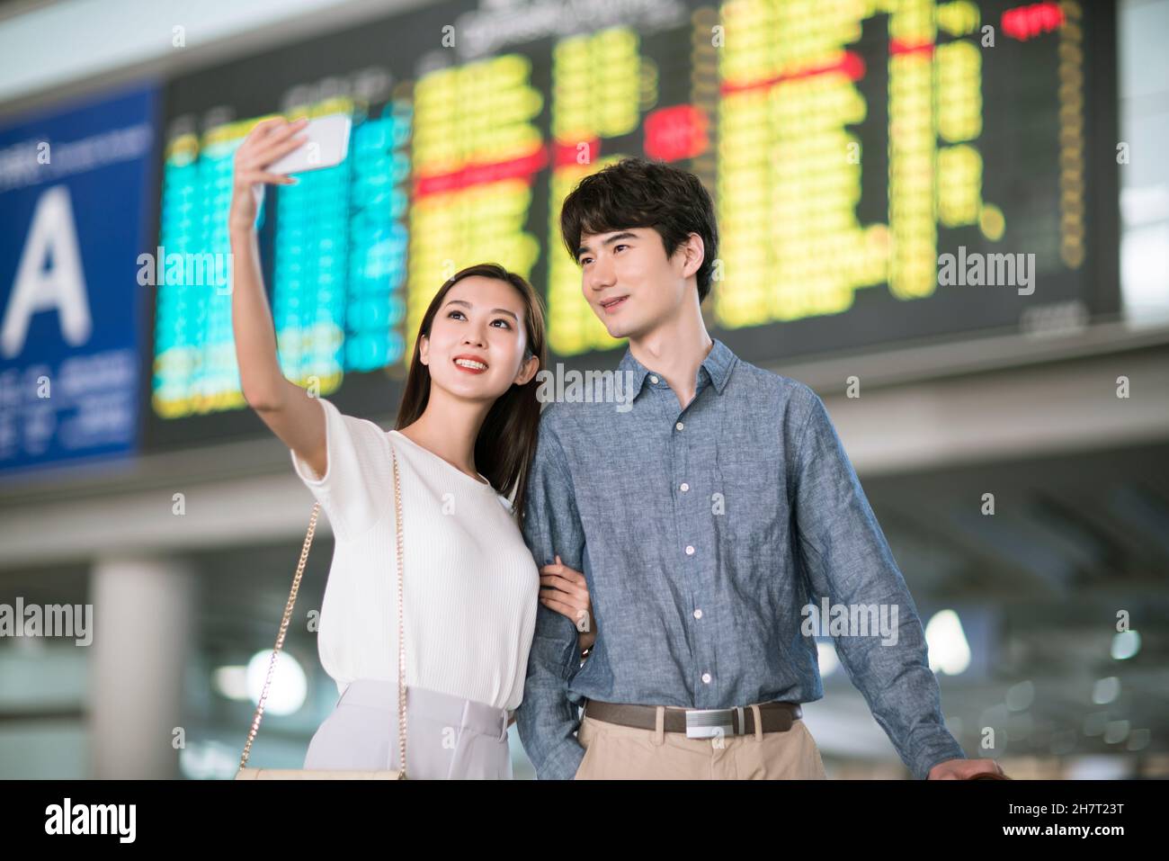 Un jeune couple prend des selfies sur son téléphone portable à la porte d'embarquement de l'aéroport Banque D'Images