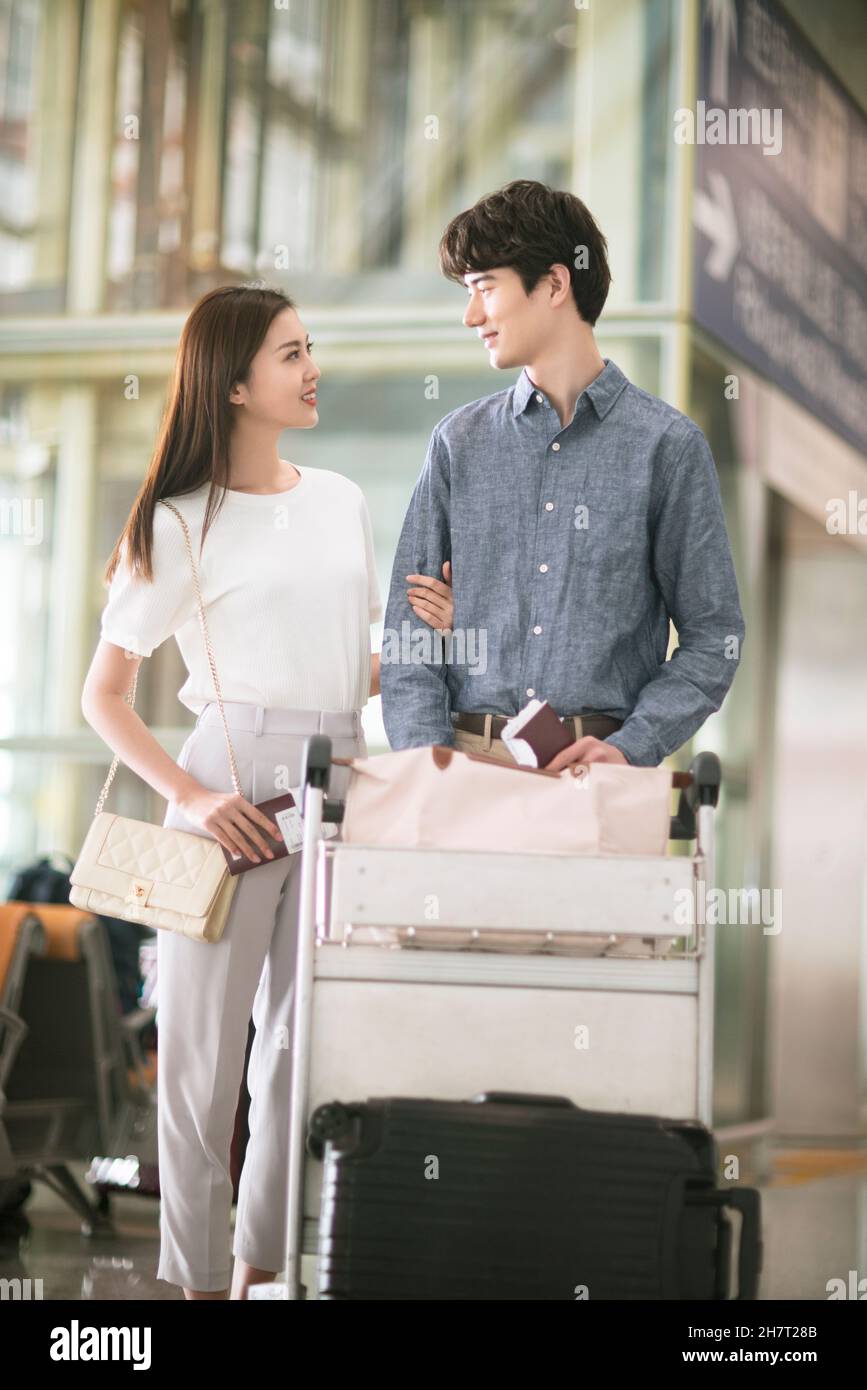 Jeune couple poussant des chariots à bagages à l'aéroport Banque D'Images