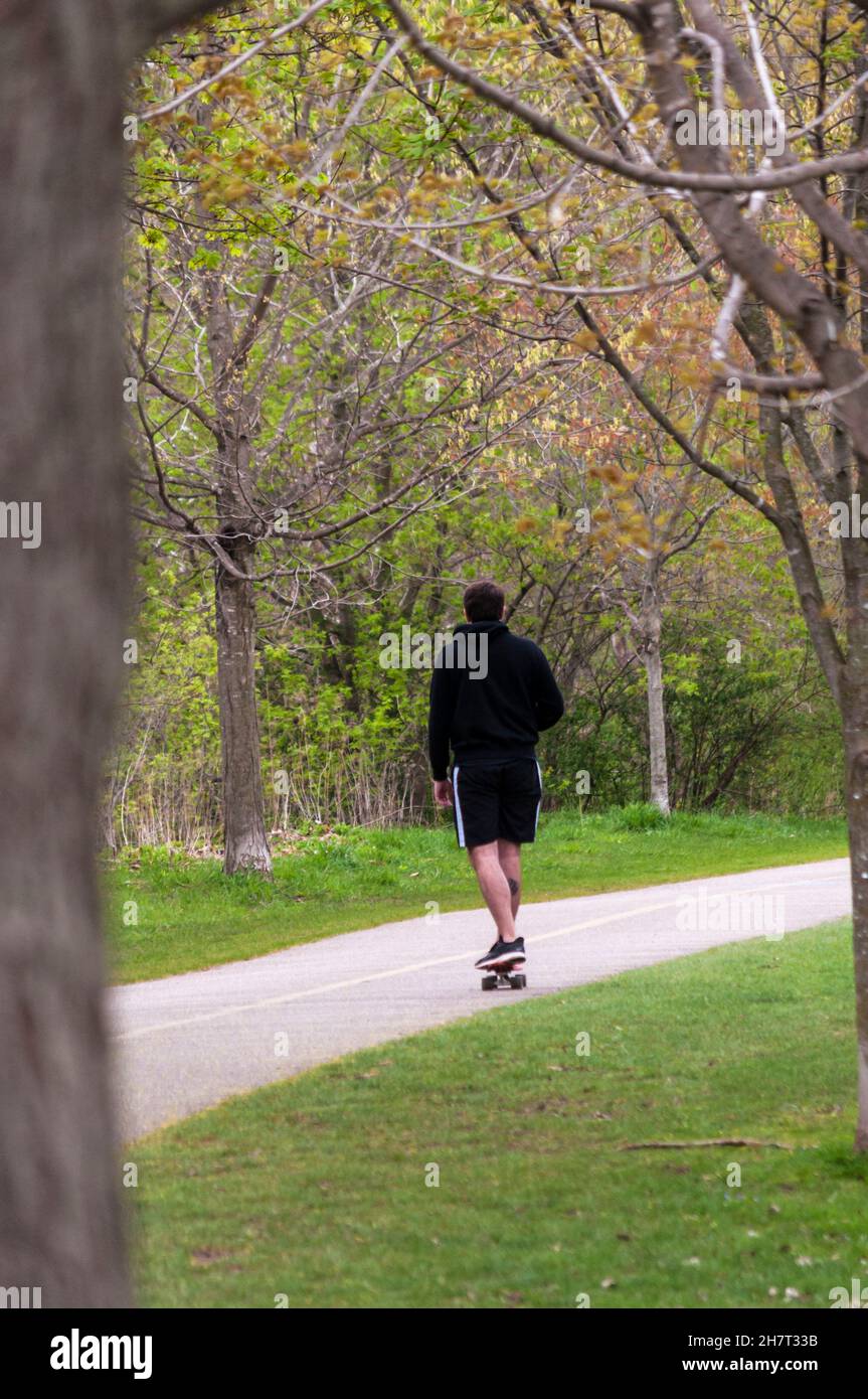Transport facile.Skate à travers un parc au début du printemps, Ontario, Canada.Les skateboarders qualifiés peuvent se déplacer rapidement, même sur les pentes, en haut et en bas Banque D'Images