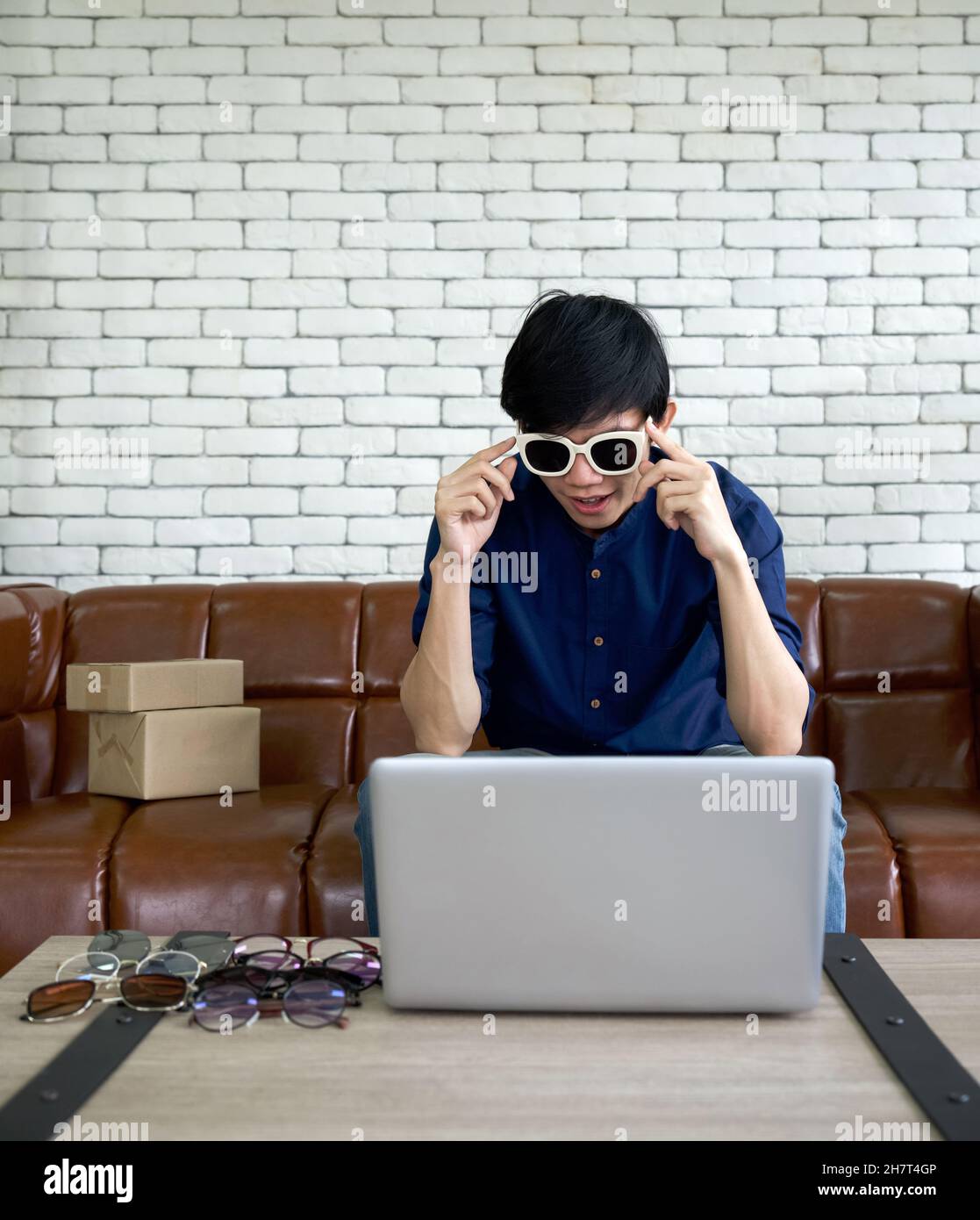 Jeune homme portant des lunettes de soleil faisant face à l'écran de  l'ordinateur.Homme asiatique vendre différents styles de lunettes en ligne  via l'application sur ordinateur portable Photo Stock - Alamy