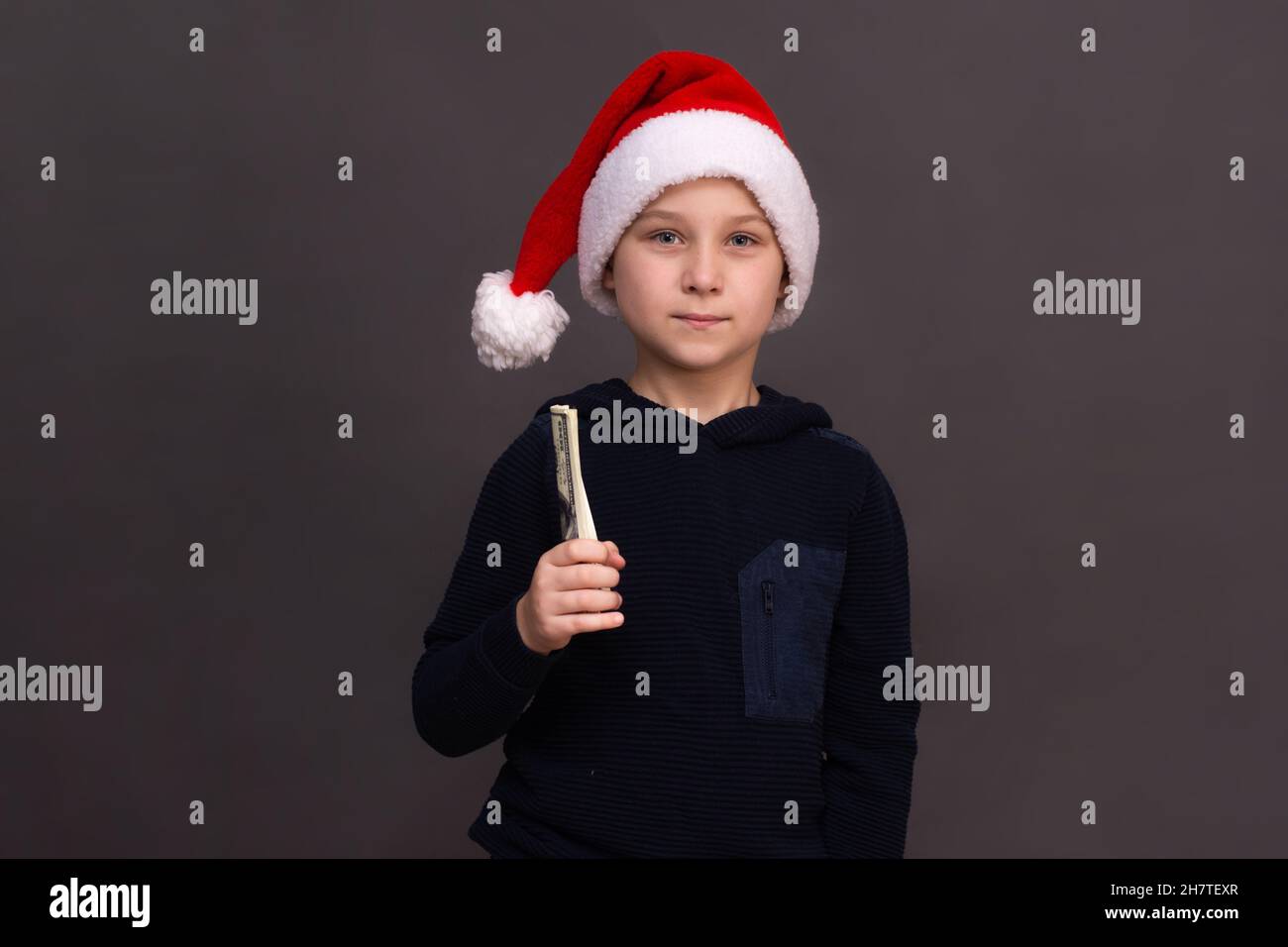 Un garçon de 8 à 10 ans dans un chapeau de Père Noël tient un paquet de billets dans sa main. Maquette Banque D'Images