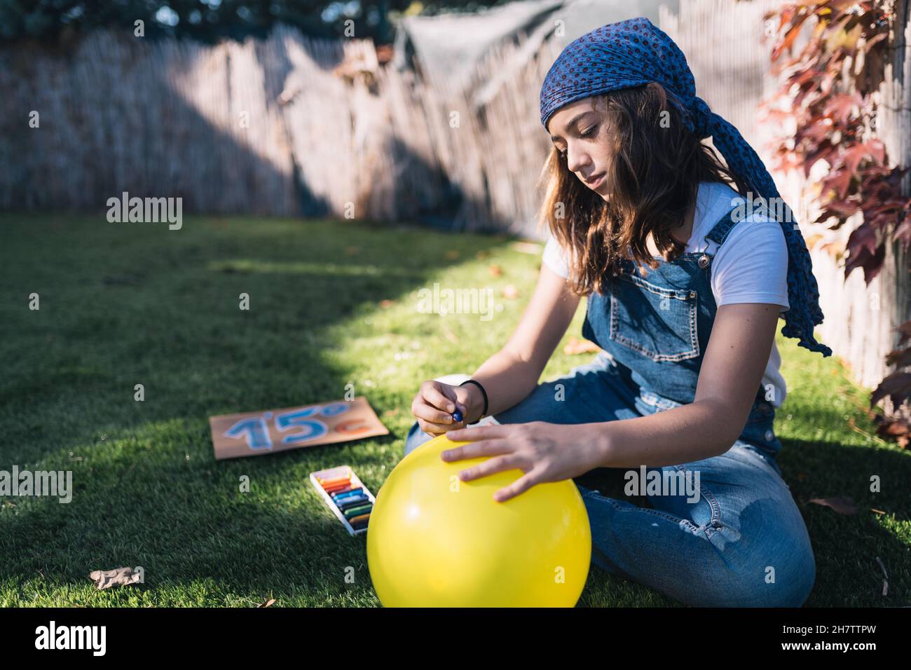 Une jeune fille activiste peint un ballon jaune dans le jardin un jour de printemps.Dessiner un appel pour empêcher la température de la terre d'augmenter de Banque D'Images