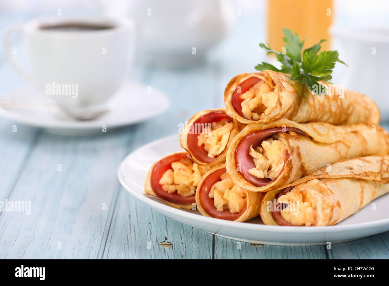 Crêpes fines faites maison avec une tranche de jambon et des œufs brouillés, empilées dans une pile, sur la table.Très bon petit déjeuner. Banque D'Images