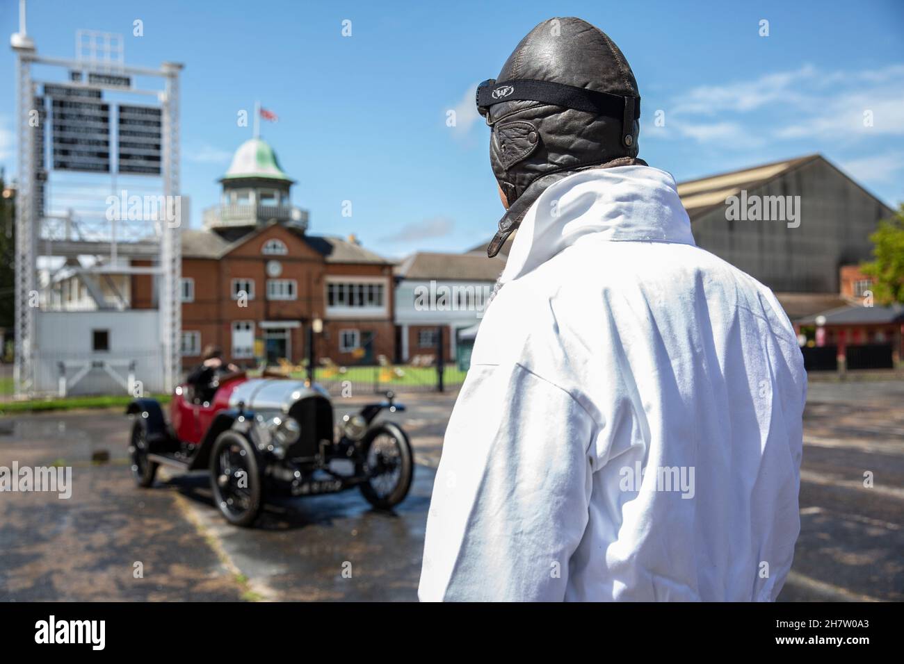 Un conducteur portant des lunettes et une combinaison vintage regardant une voiture Bentley classique à Brooklands, le premier circuit de course au monde, l'Angleterre. Banque D'Images